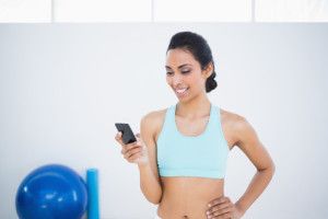 Cute sporty woman using her smartphone standing in sports hall